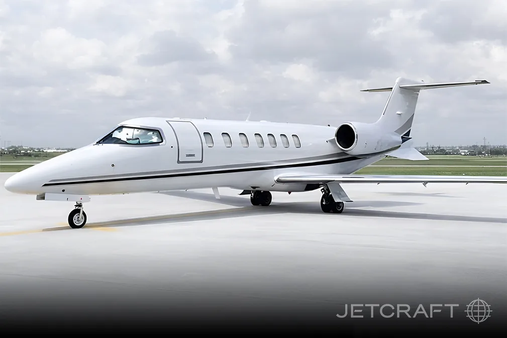 A white business jet with a black and grey stripe on the tarmac under a cloudy sky.