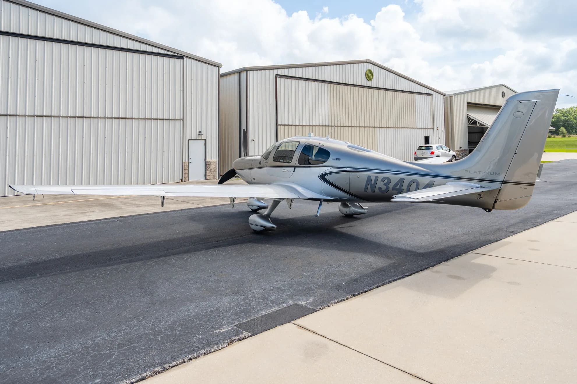 Side view of a silver Cirrus SR22T aircraft (N3404) parked on an airport tarmac with hangars in the background.