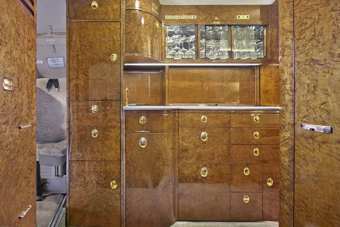 The galley area of a private jet featuring extensive polished wood cabinetry and storage.