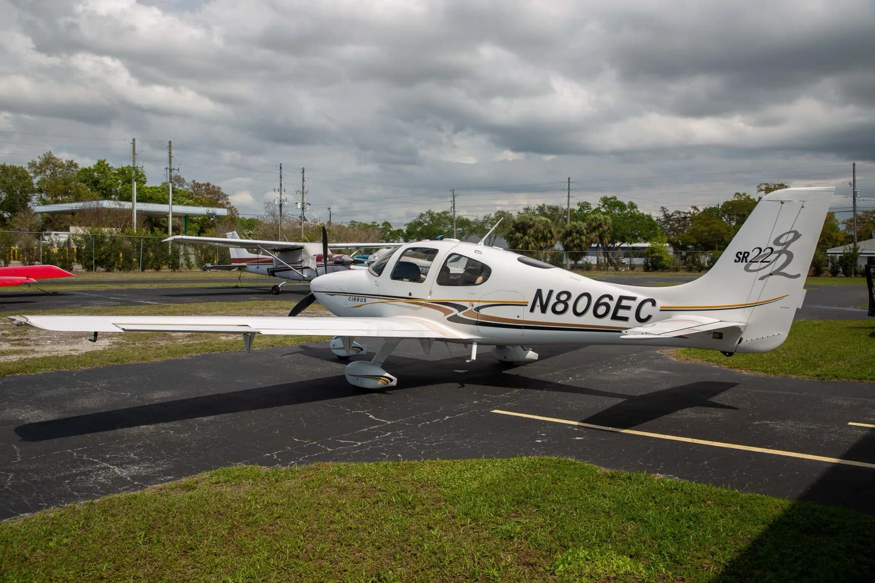 A white Cirrus SR22 aircraft with black and gold stripes, registration N806EC, parked on an asphalt tarmac.