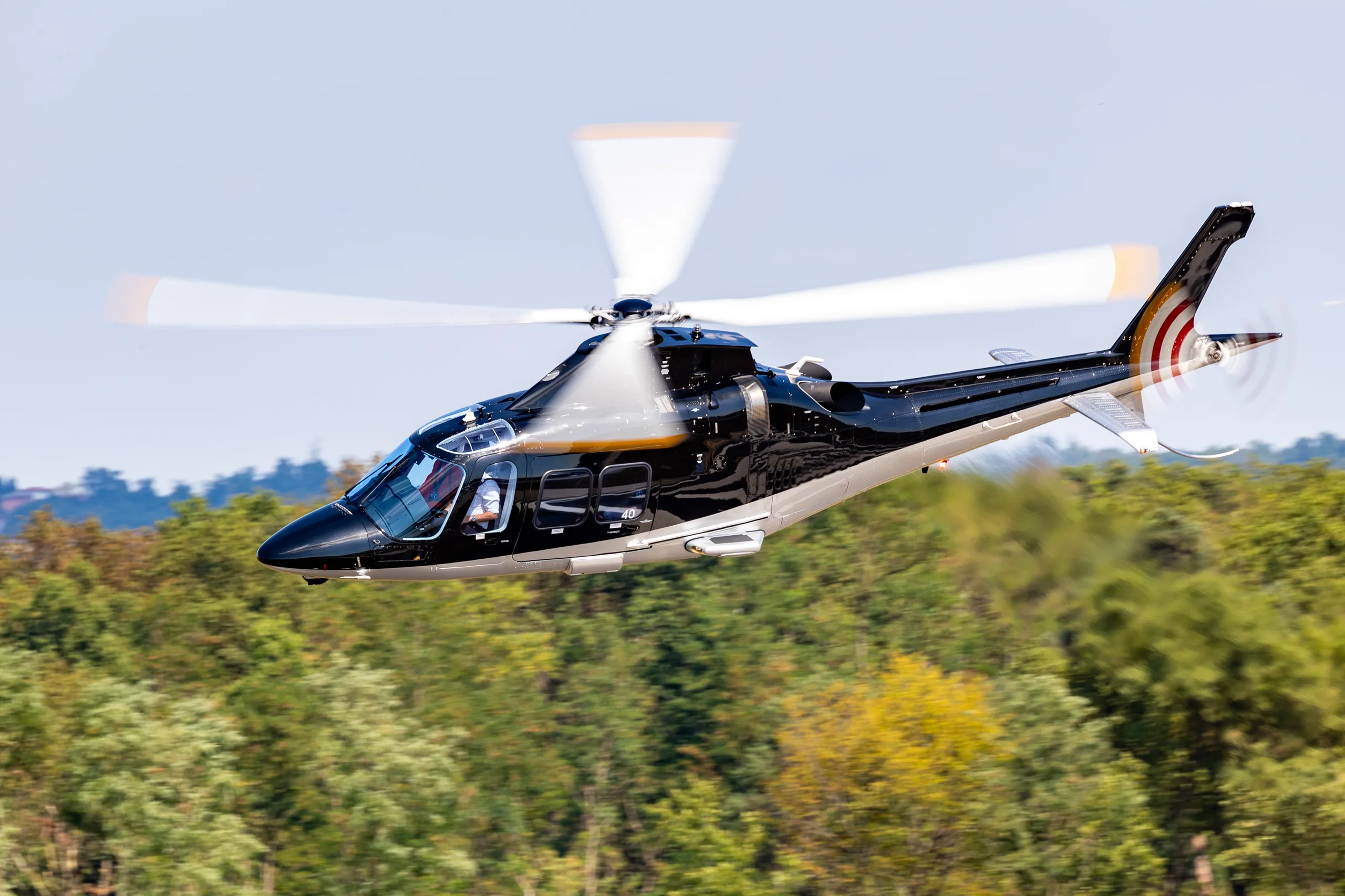 A black and silver helicopter in flight over a green forest.