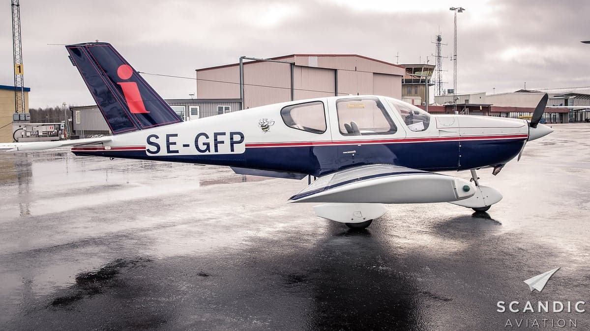 A blue and white aircraft is parked on a wet tarmac near a building.