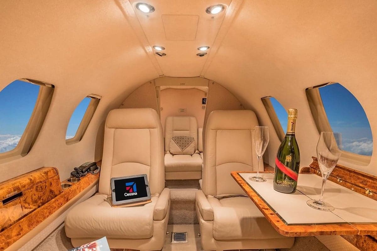 The elegant cabin interior of a private jet featuring beige leather seats, a table with champagne, and a tablet.