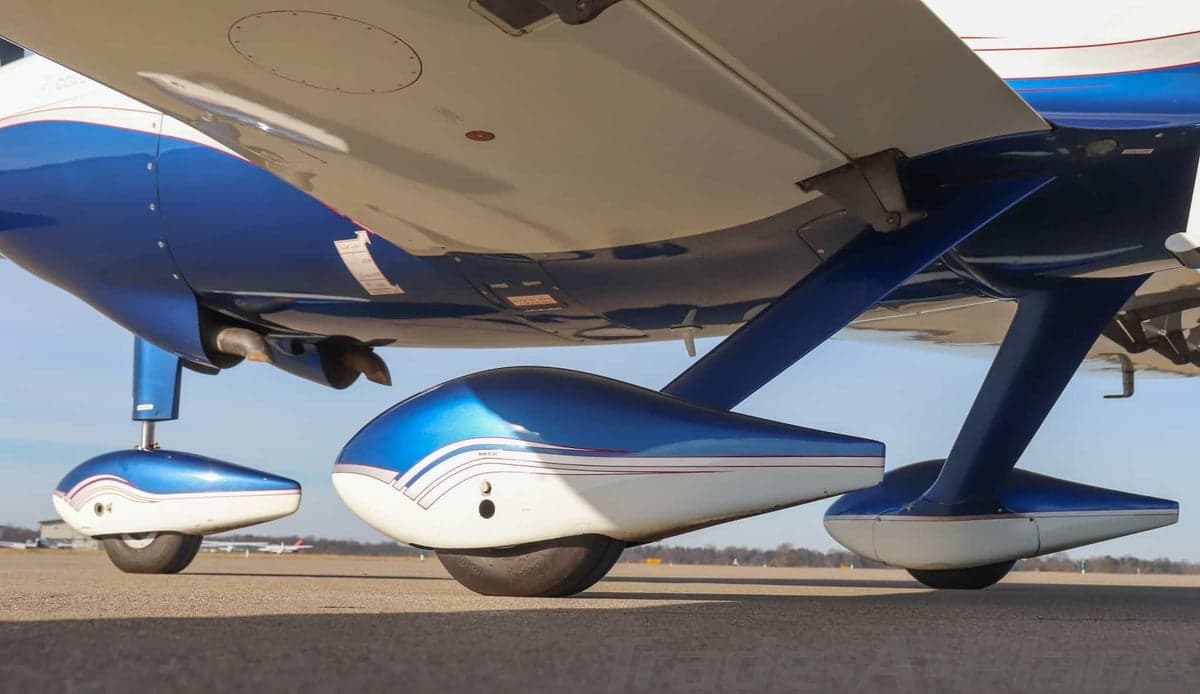 Close-up view of the blue and white main landing gear and underside of a Columbia 400 aircraft wing.