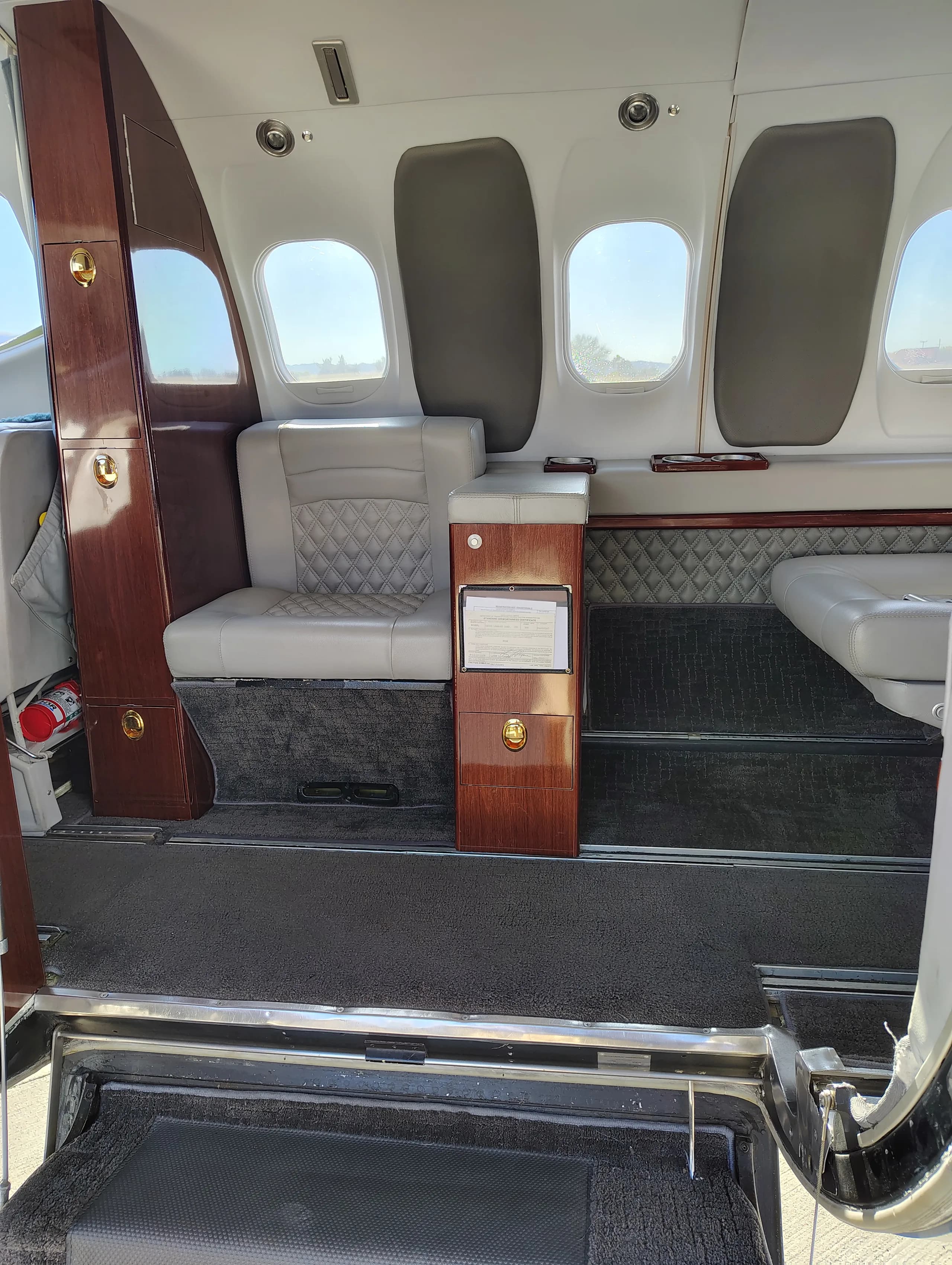 View of the aircraft cabin interior from the entry steps, showing light gray seats and wood accents.