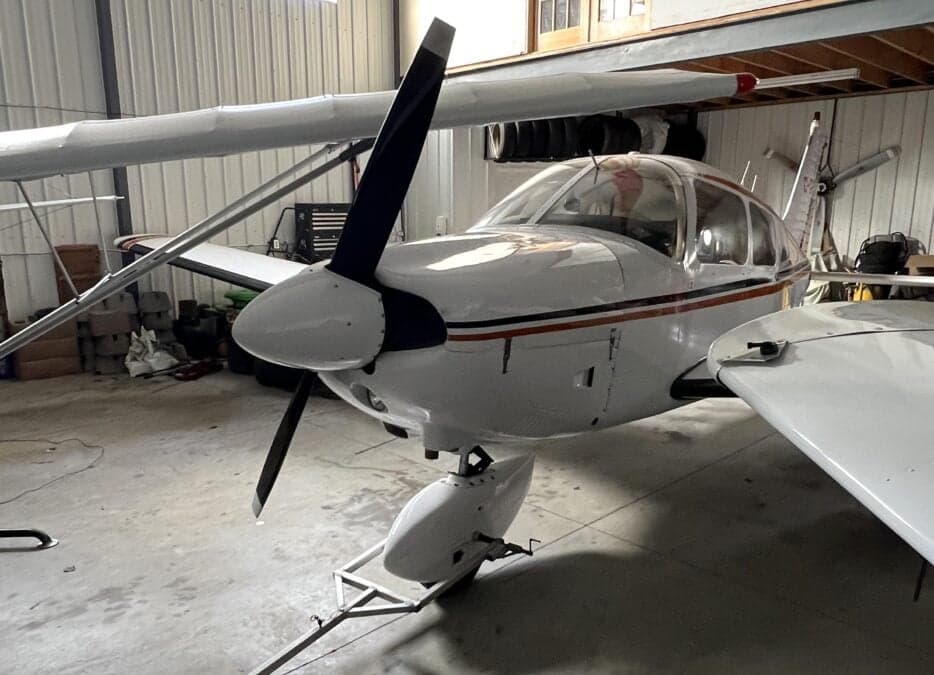 Front view of a white and orange aircraft with a black propeller in a hangar.