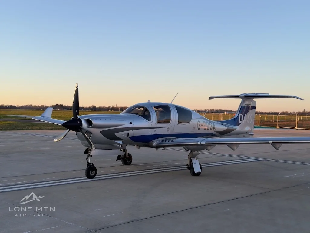 A front quarter view of a silver and blue Diamond DA50 aircraft with registration G-DOGA parked on an airfield.