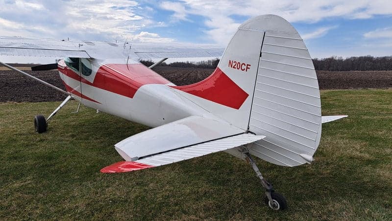 A rear quarter view of the red and white Cessna on a grassy field.