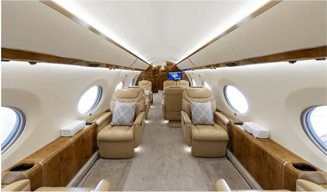 The private jet's spacious interior cabin with multiple beige leather seats and large windows.