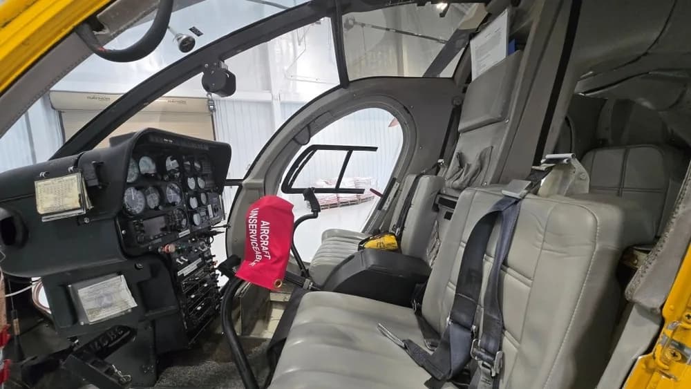 The cockpit and front cabin of the yellow helicopter, showing the instrument panel and grey seats.