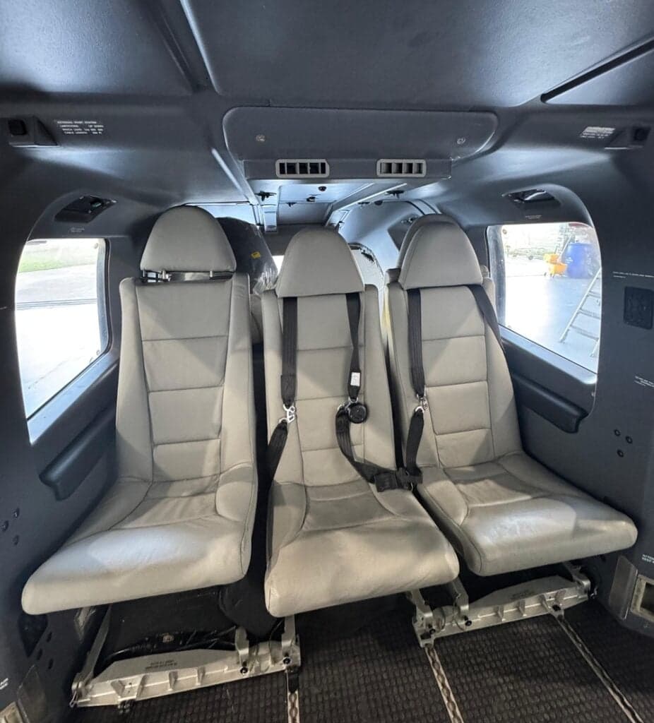 Helicopter cabin with three gray seats and seatbelts.