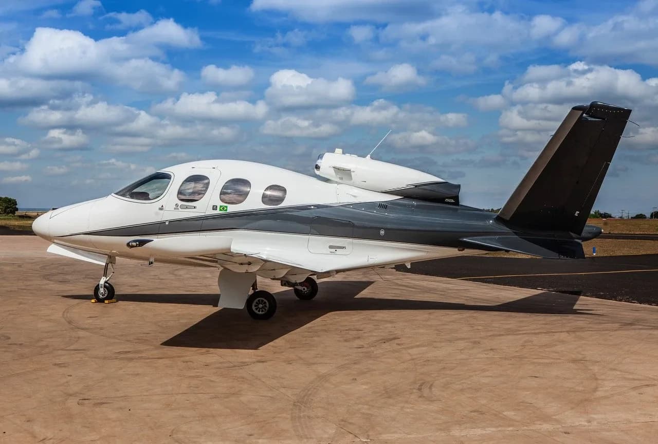 A side view of a white and dark grey Cirrus Vision Jet parked on a light brown tarmac.