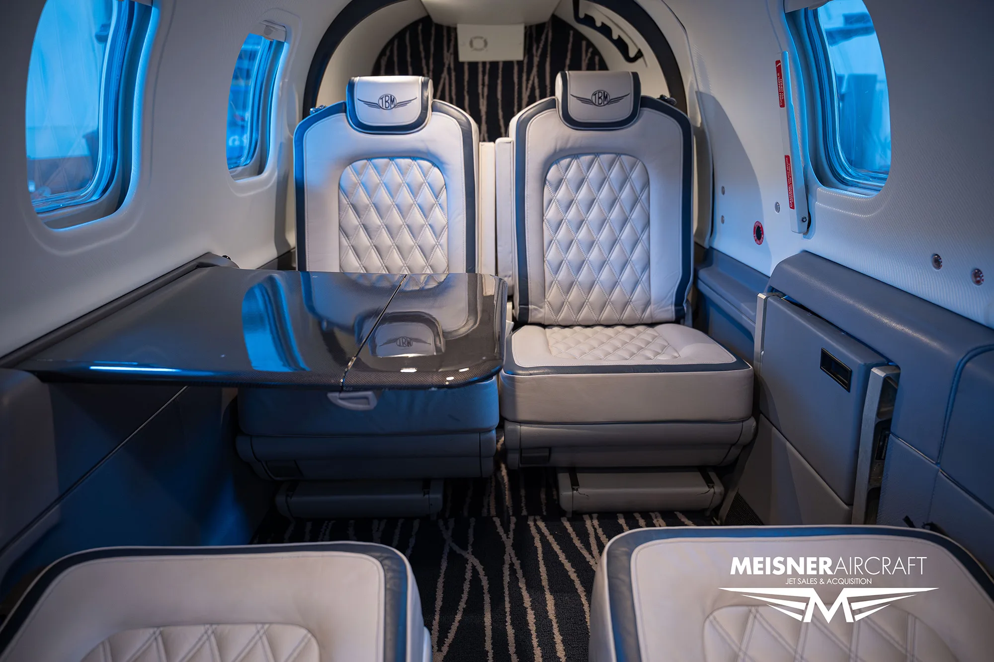 The interior cabin of an aircraft, featuring two quilted leather seats and a small table between them.
