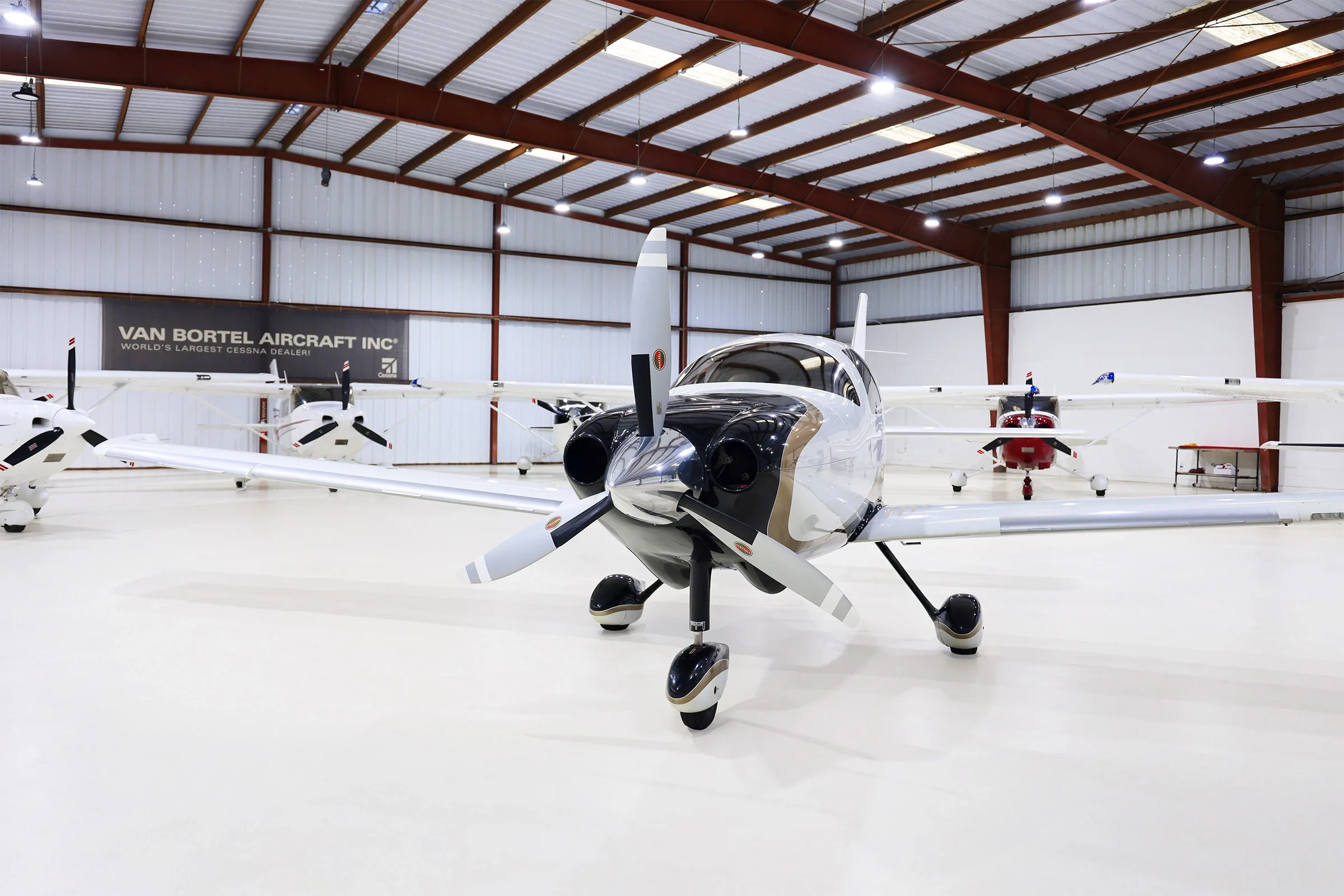 A white, black, and gold Cessna TTx aircraft (N384AD) is parked in a hangar, viewed from the front.