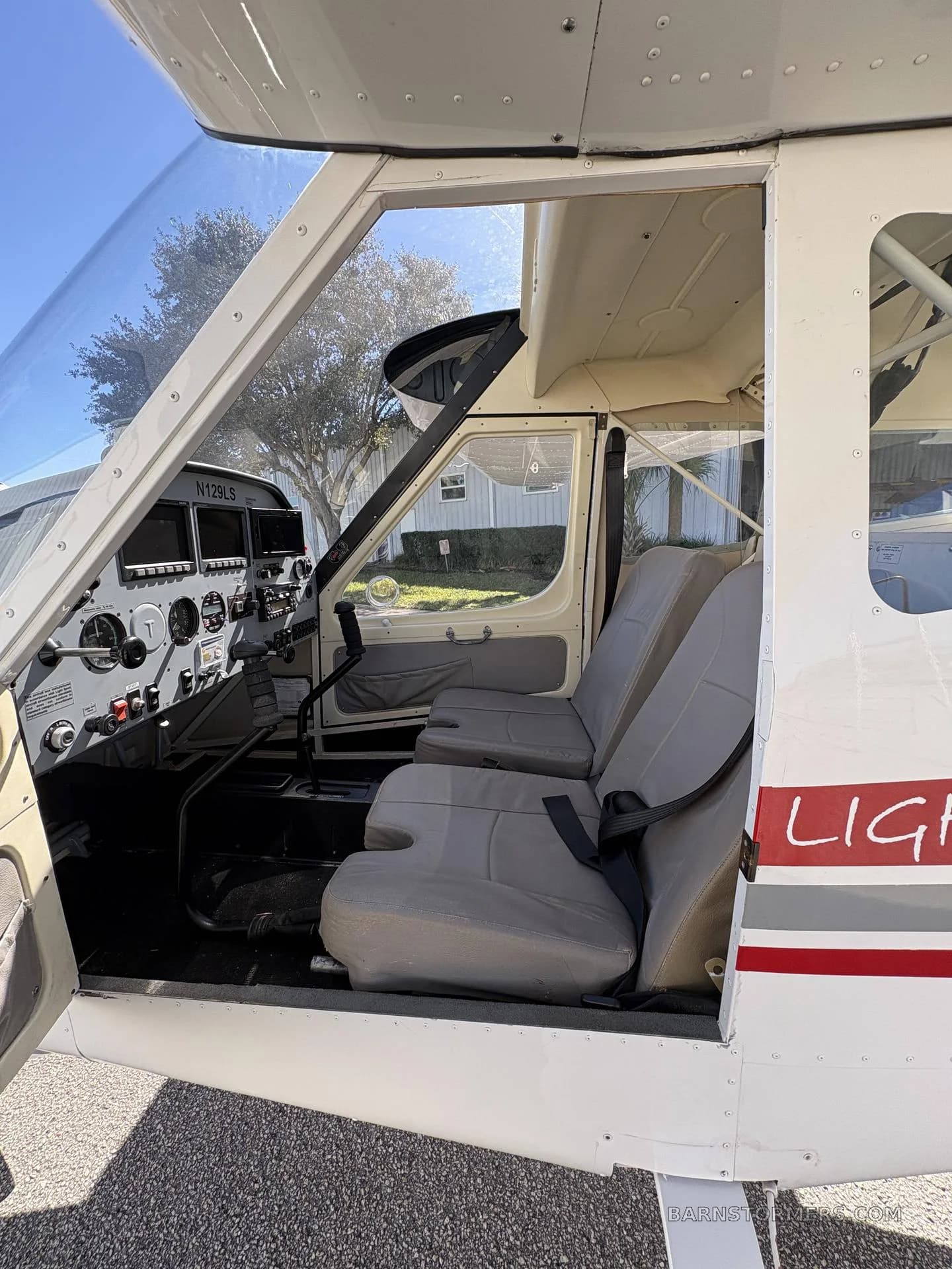 The interior of a white and red Tecnam P2008 aircraft shows two grey seats and the instrument panel through an open door.