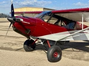 Close up of the front of a red and white Carbon Cub aircraft on the ground.