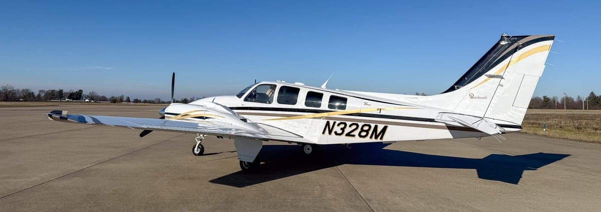Side view of a white twin-engine propeller aircraft N328M with black and gold stripes on an airfield.