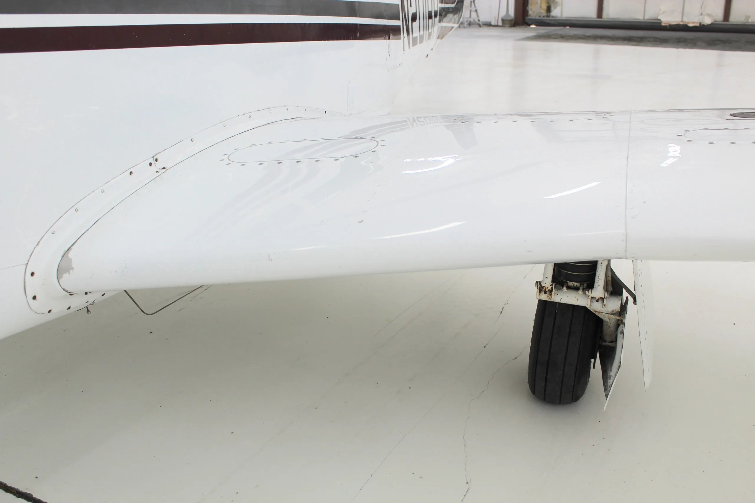 Close up of the wing and landing gear of the white and brown N201BP aircraft in a hangar.