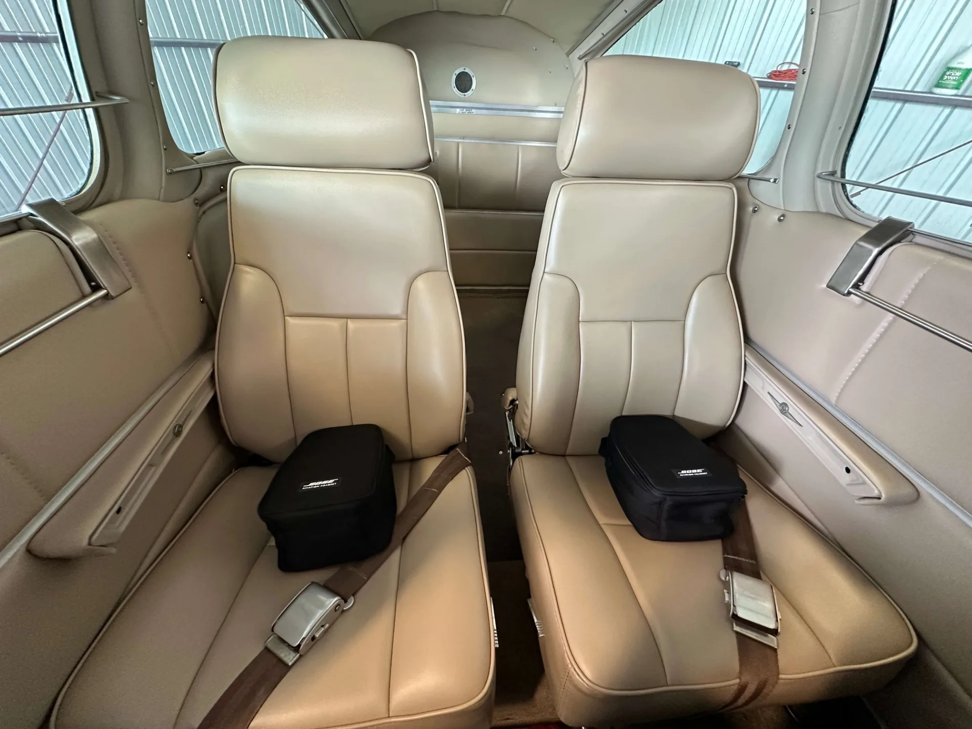 The tan leather interior cabin seats of a Beechcraft Bonanza, with two black bags on the front seats.