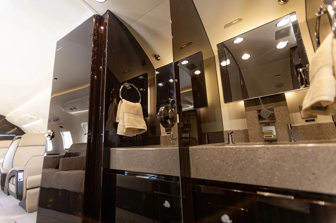 The lavatory of a business jet, featuring two sinks, large mirrors, and dark wood accents.