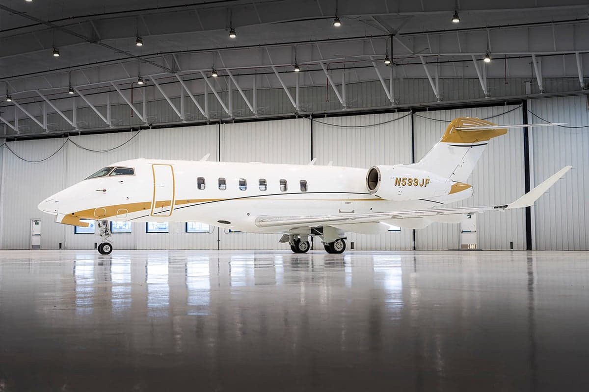 Side view of a white and gold Challenger aircraft with registration N599JF in a hangar.