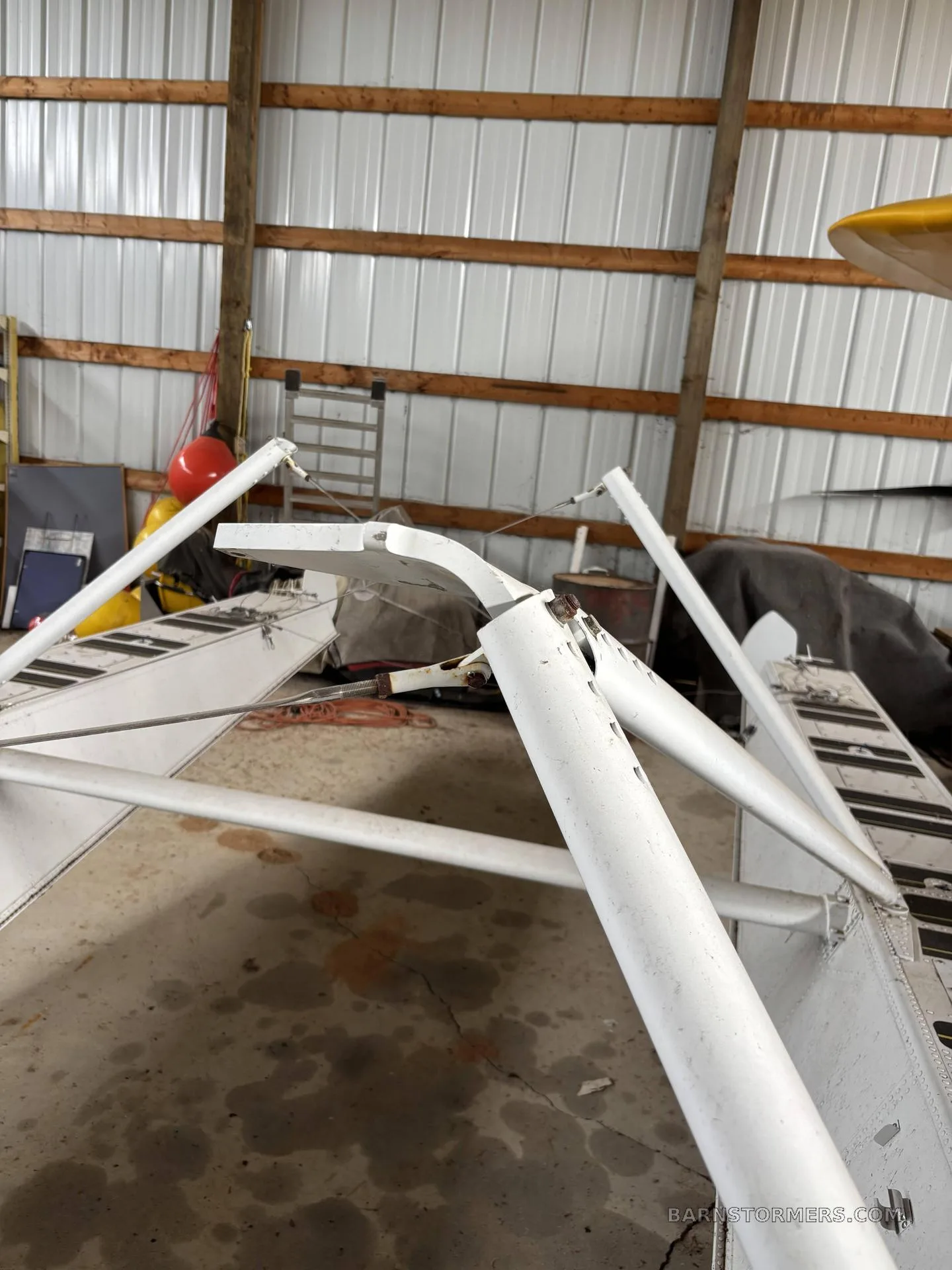 A view of the white support struts connecting to an aircraft float, with other aircraft components and hangar walls in the background.