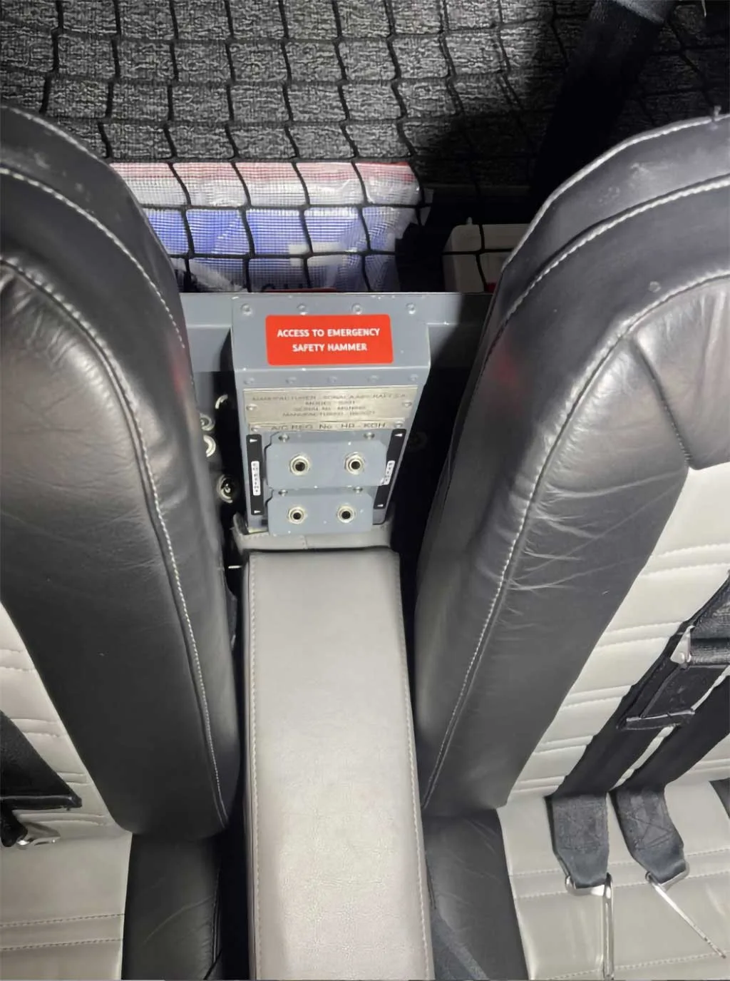 Close-up view between the aircraft seats showing a storage compartment and an "ACCESS TO EMERGENCY SAFETY HAMMER" label.