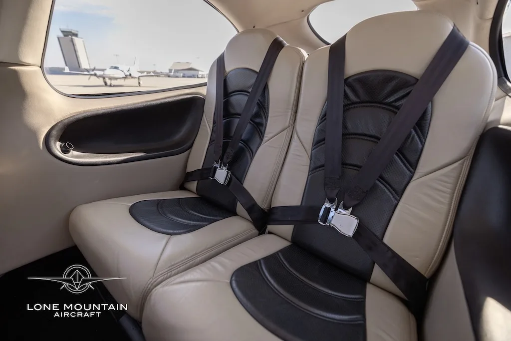 A side view of the tan and black leather rear seats of a Cirrus SR22 aircraft cabin, with an airport tower visible outside.
