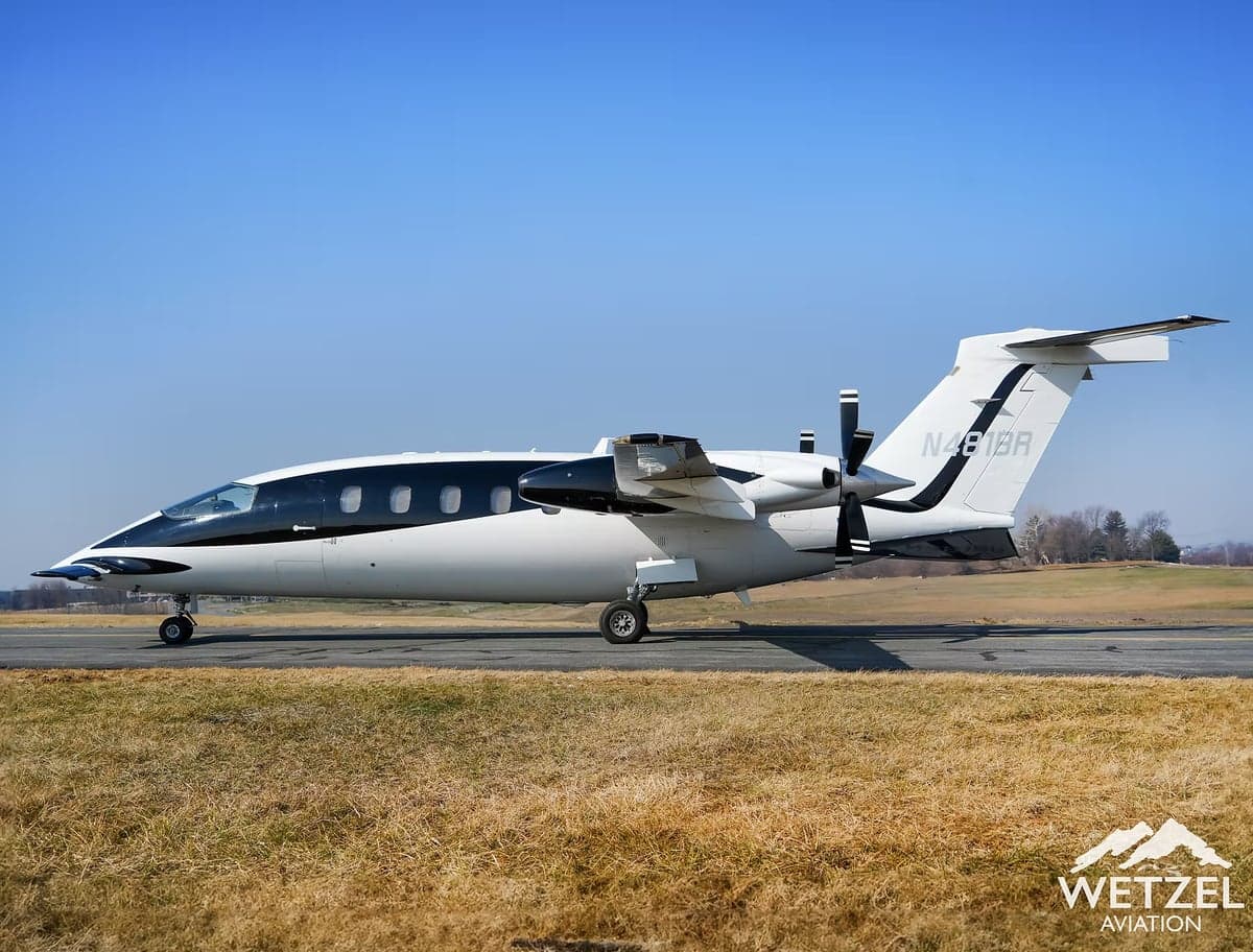 A Piaggio Avanti EVO aircraft is parked on the tarmac with a blue and white paint scheme, showing the registration number N481BR.