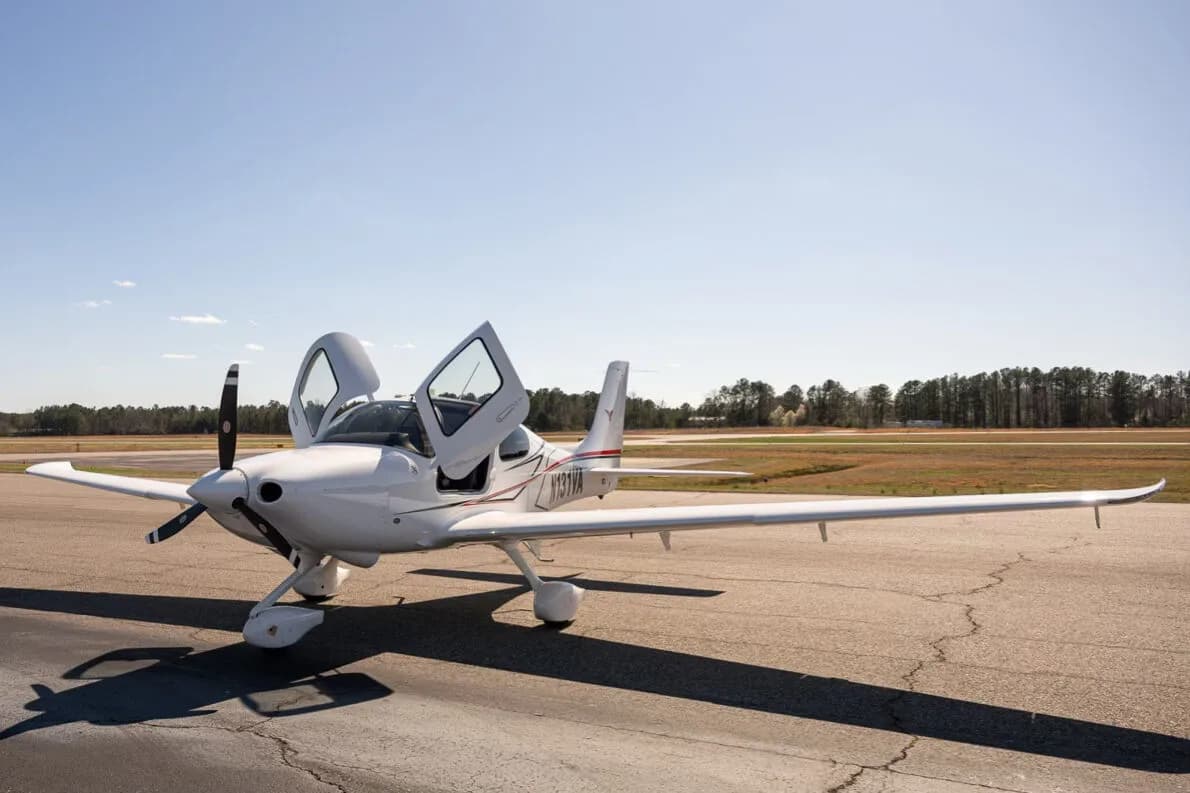 A white Cirrus SR22 aircraft with red and black accent stripes, tail number N131VA, parked on an airfield with both doors open.