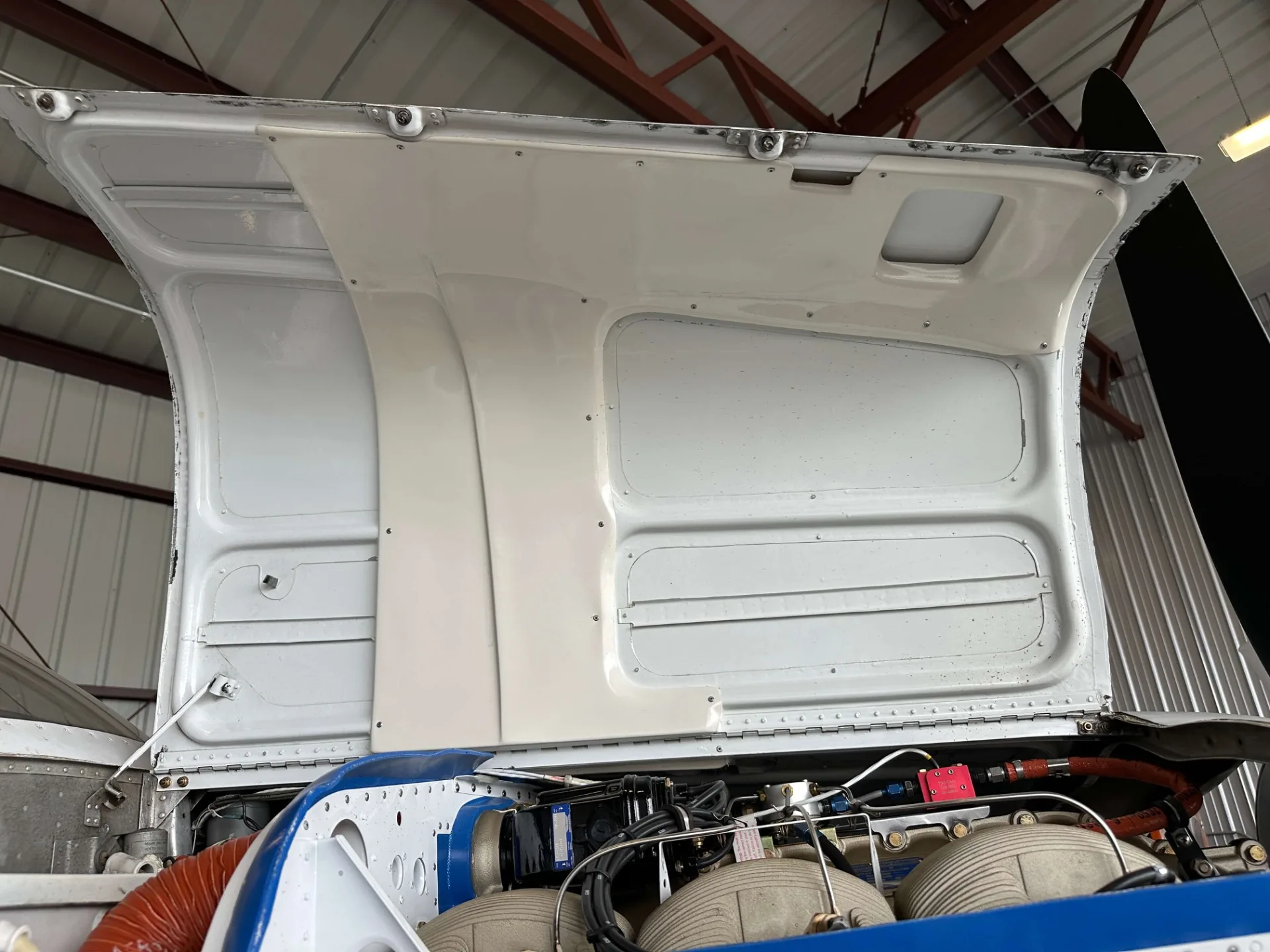 The engine cowling of a Beechcraft Bonanza opened, revealing the underside of the cowling and the top of the engine compartment.