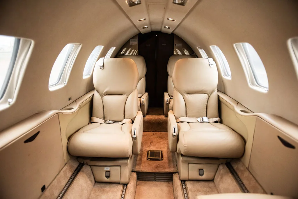 A private jet's beige leather cabin interior showing multiple passenger seats and the central aisle.