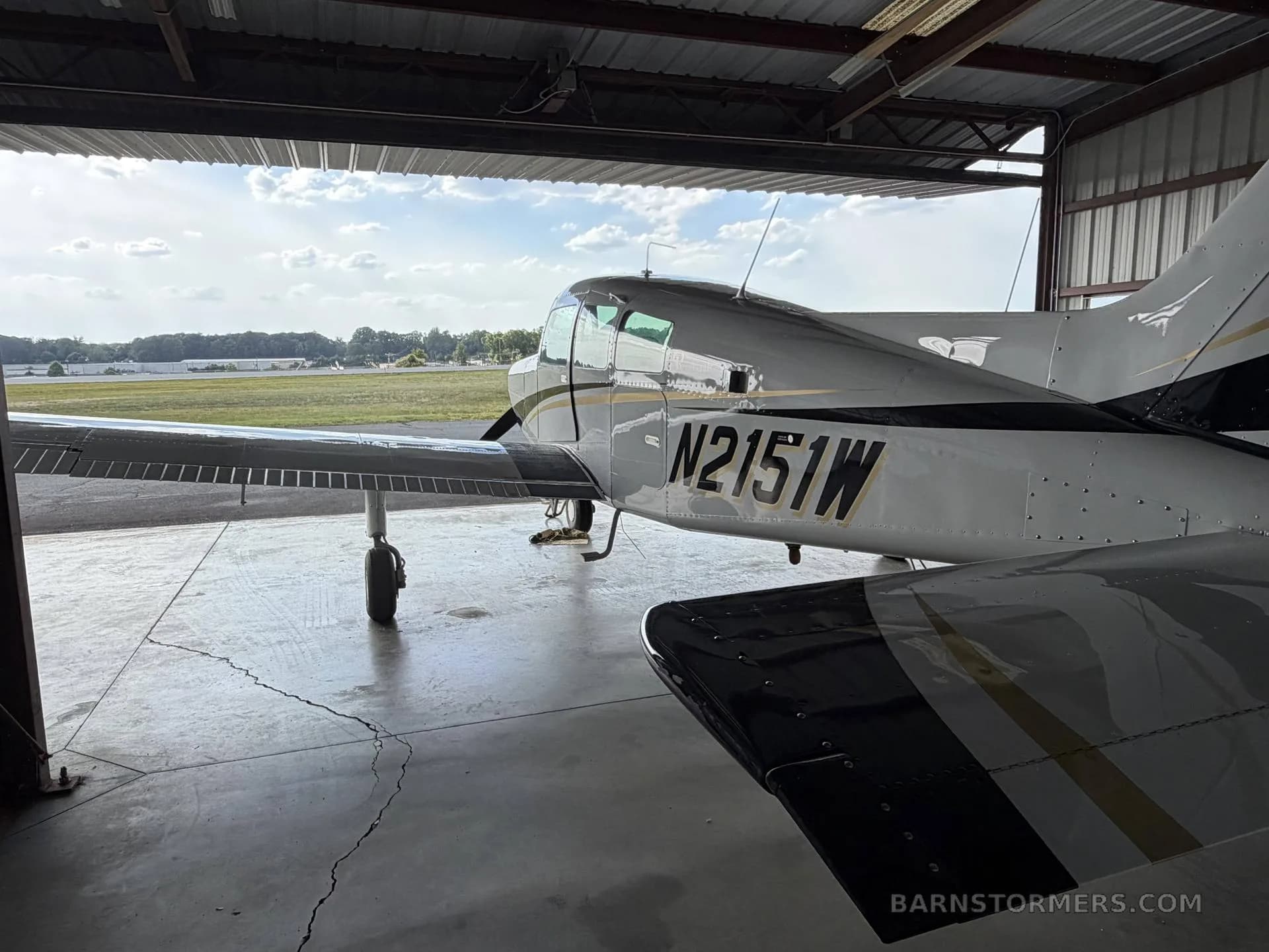 The tail and wing of a white and black single-engine aircraft, N2151W, partially inside a hangar with an airfield visible outside.