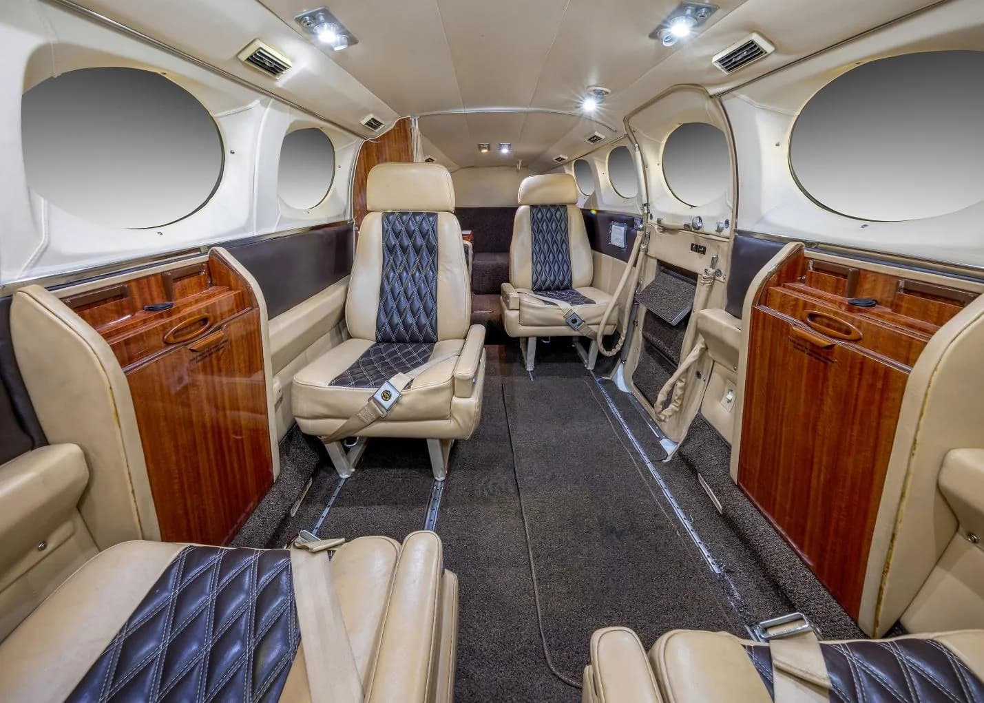 The aircraft cabin interior with beige and black quilted seats and wood paneling, looking towards the rear.