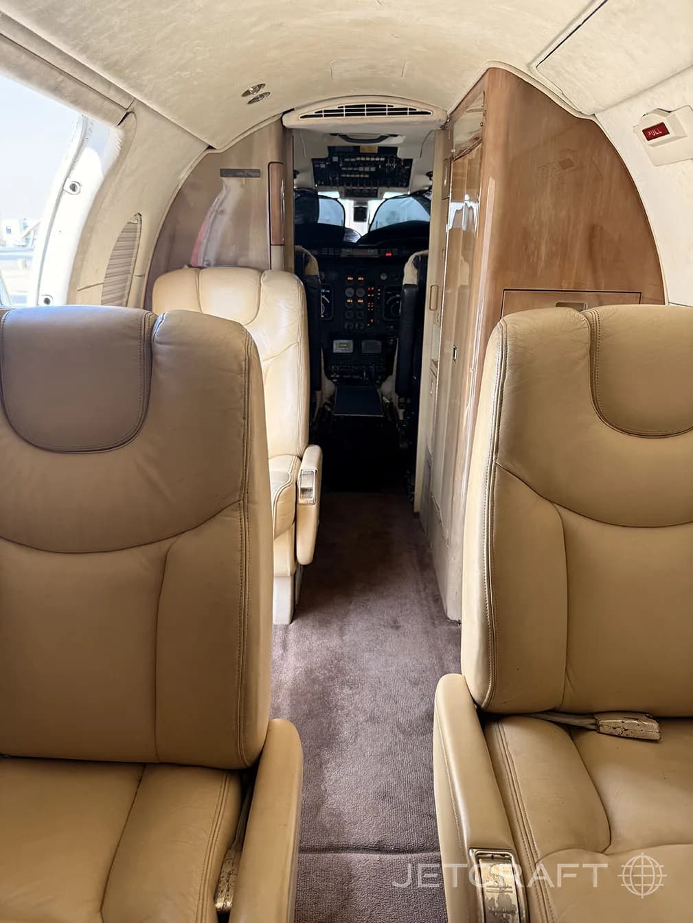 The interior cabin of a private jet with tan leather seats and a view into the cockpit.