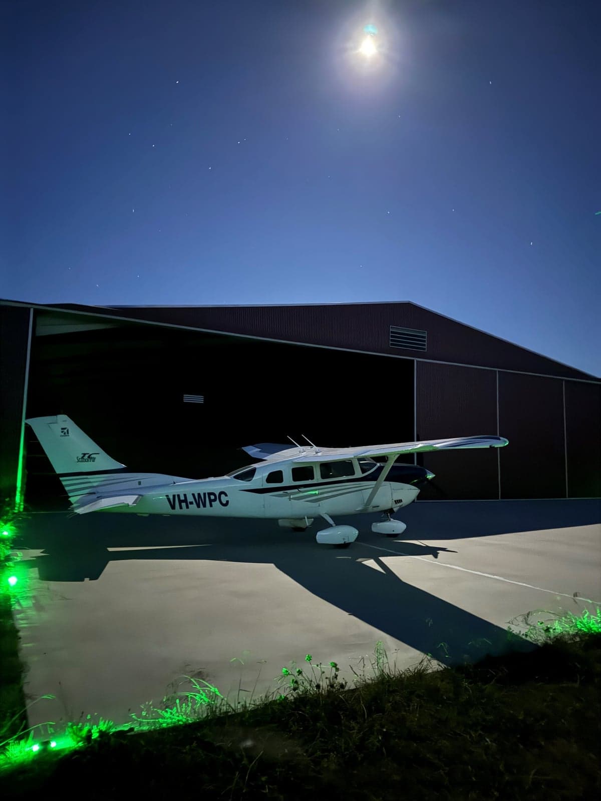 Cessna aircraft parked outside a hangar at night under a full moon.