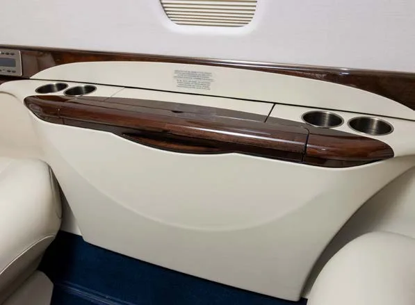 A close-up of a business jet's cabin side panel with cup holders and a dark wood trim.