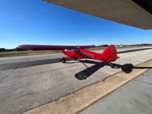 A red aircraft is parked on the tarmac under a blue sky.