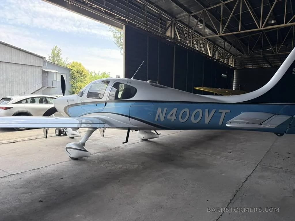 A white and blue Cirrus SR22 aircraft, registration N400VT, is parked inside a hangar with its door open.