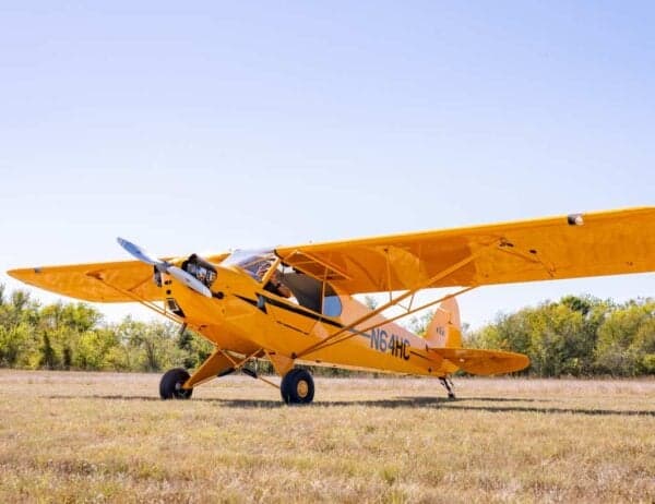 A yellow Legend Cub aircraft, registration N64HC, is parked on a grassy field under a clear blue sky.