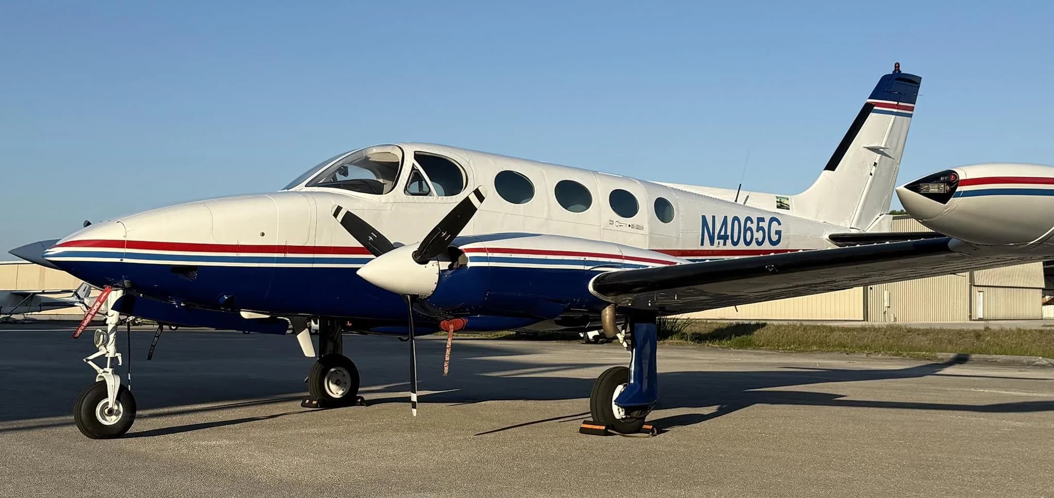 A white and blue twin-engine propeller aircraft, a Cessna 414 Chancellor with registration N4065G, parked on an asphalt ramp under a clear sky.