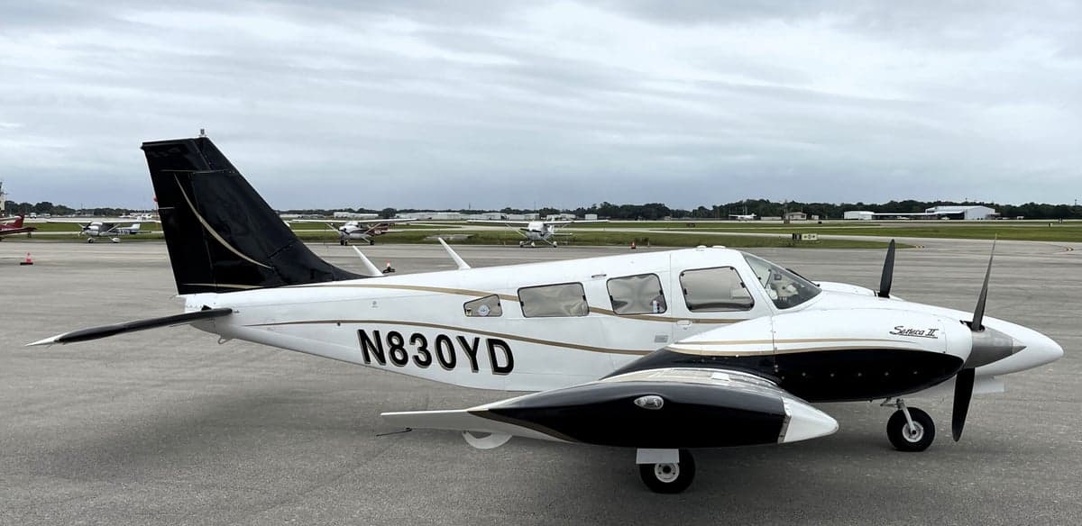 A Piper Seneca II aircraft with a white and black paint scheme is parked on the tarmac.