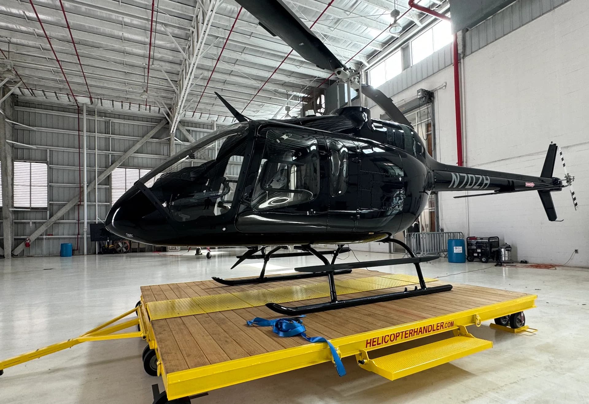 A black helicopter with registration N770EH sits on a yellow trailer inside a hangar.