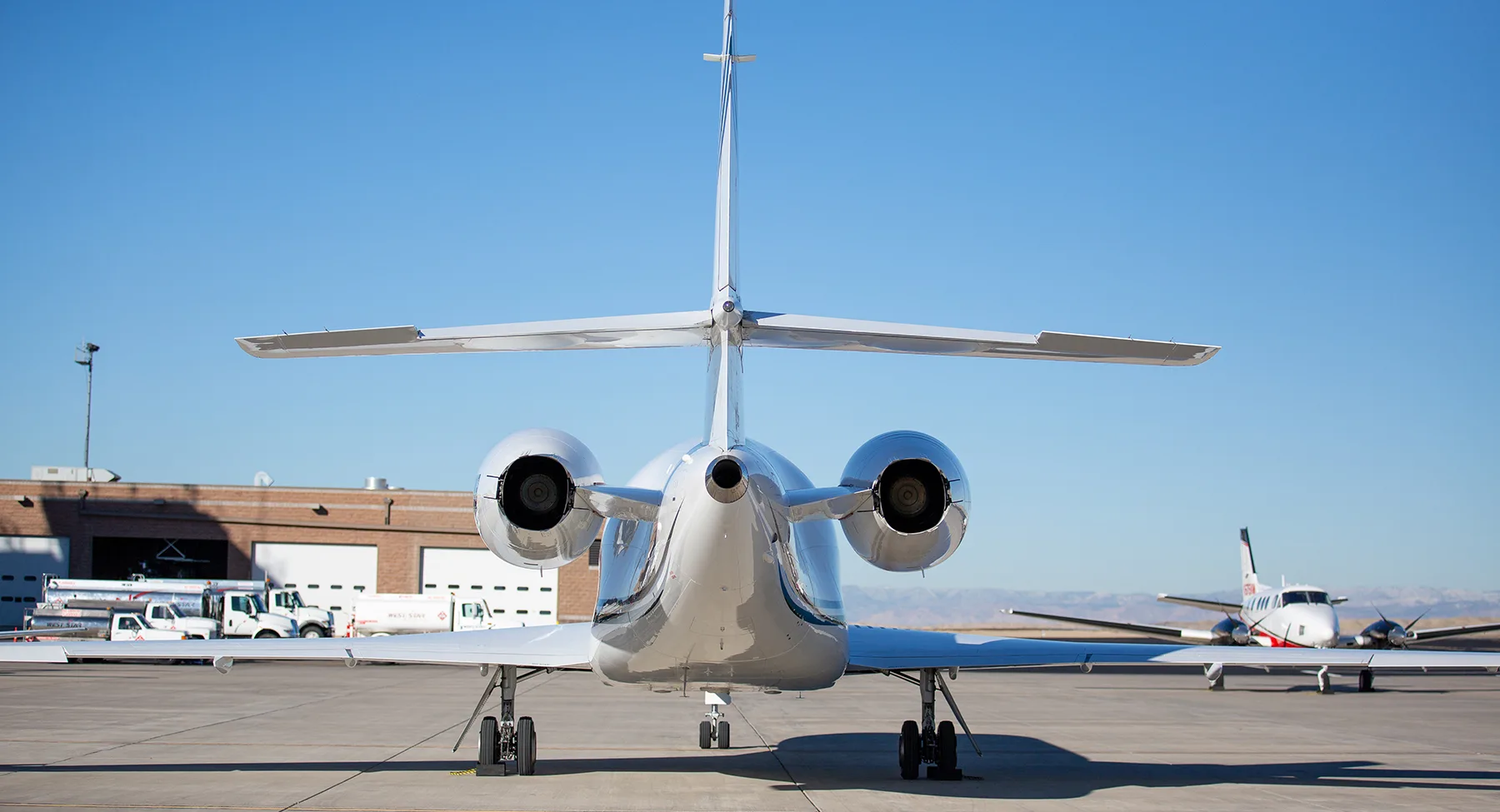 A rear view of a white business jet with two tail-mounted engines, parked on an airfield on a clear day.