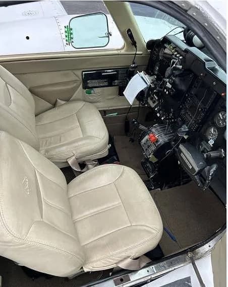 The aircraft's front cabin showing light-colored leather pilot and co-pilot seats and a partial view of the cockpit controls.