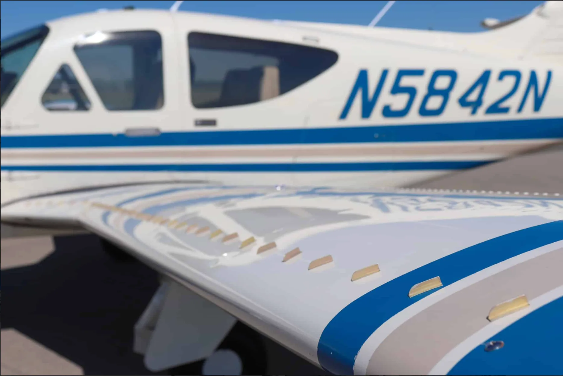 Close-up view of the wing and fuselage of a white aircraft with blue and tan stripes, showing registration N5842N.
