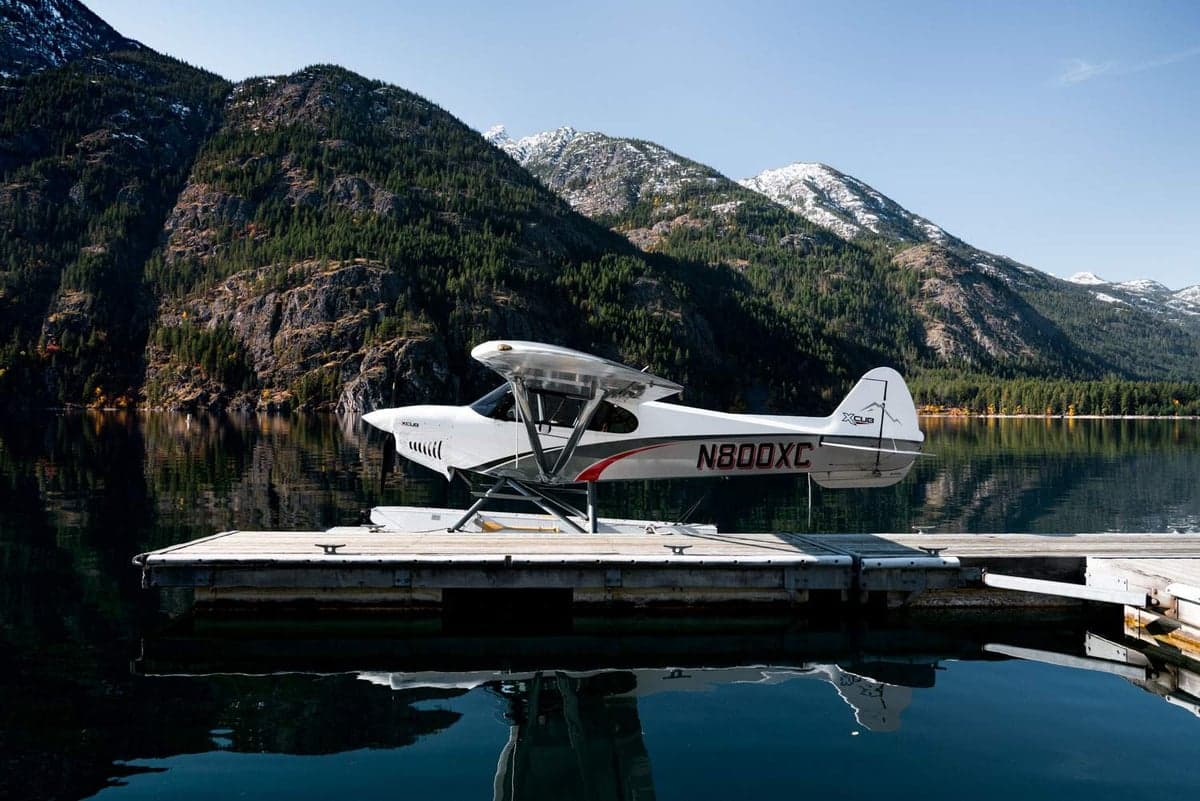 An XCub seaplane is docked on a lake with mountains in the background.