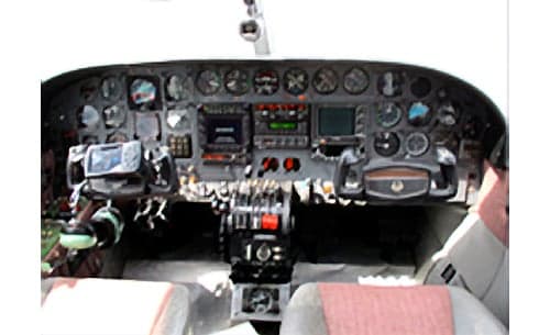 A detailed view of a twin-engine aircraft cockpit, featuring the instrument panel, controls, and front seats.