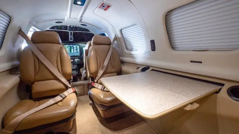 A wider view of the tan leather interior cabin of a Piper M-class aircraft, showing passenger seats and a side table.