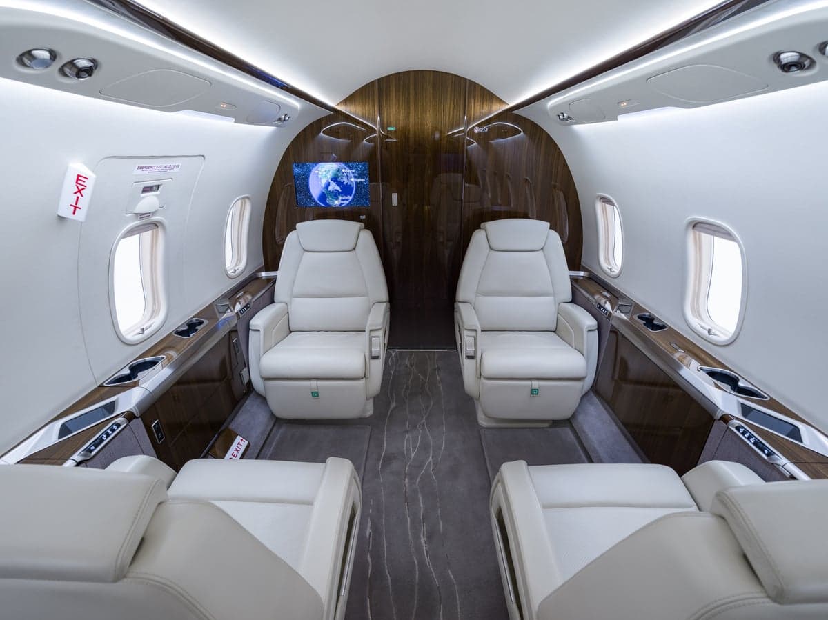 View of the aircraft's interior with white leather seats and wood trim.